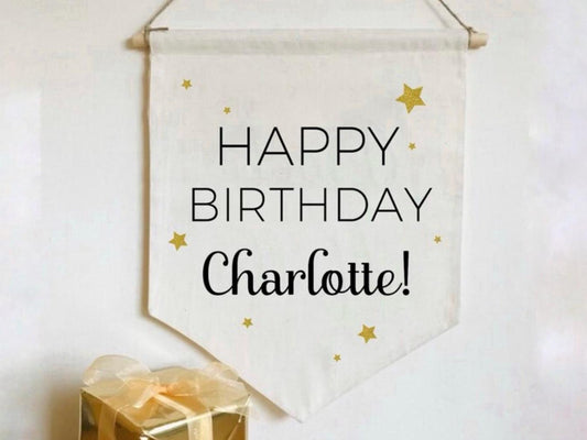 a natural coloured canvas banner printed with Happy Birthday and personalised with a name. Surrounded by gold glitter stars