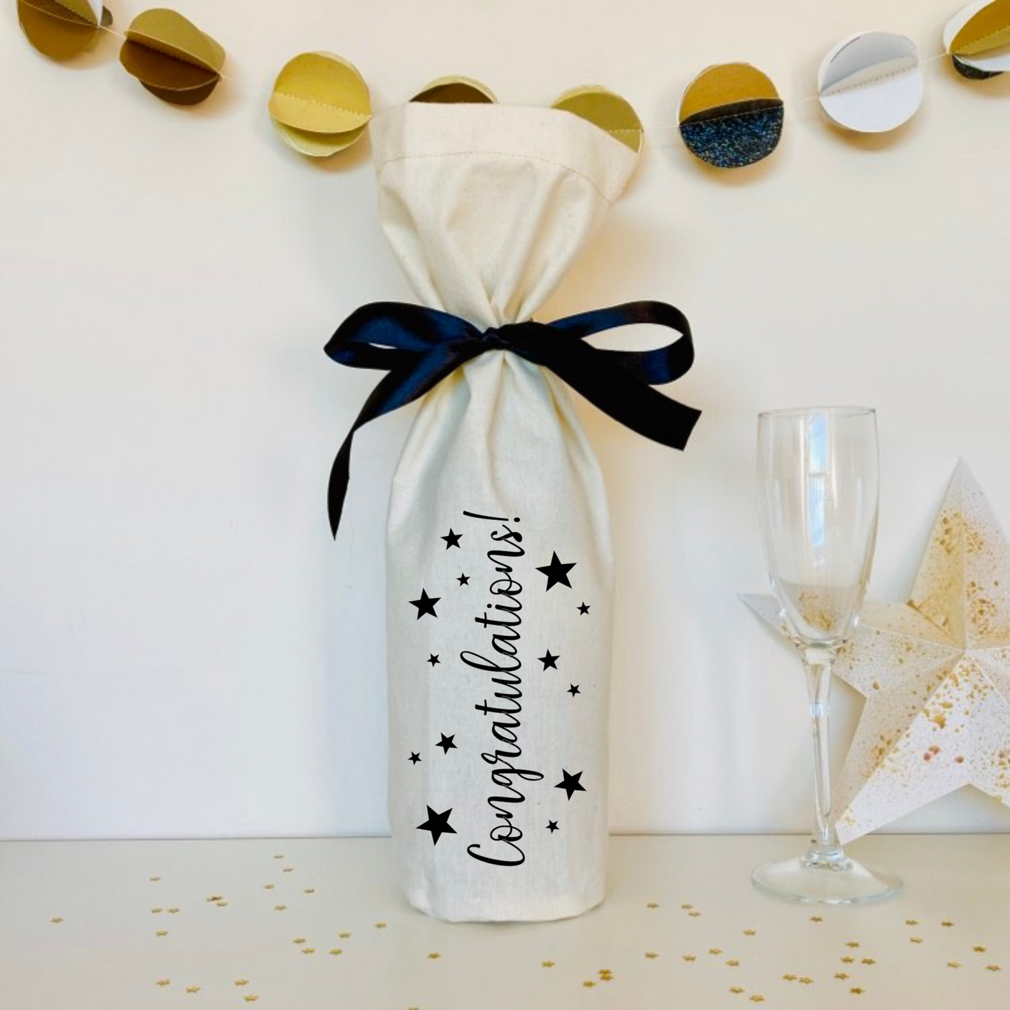 a calico bottle bag printed with Congratulations! and decorated with stars. Tied with a black satin ribbon