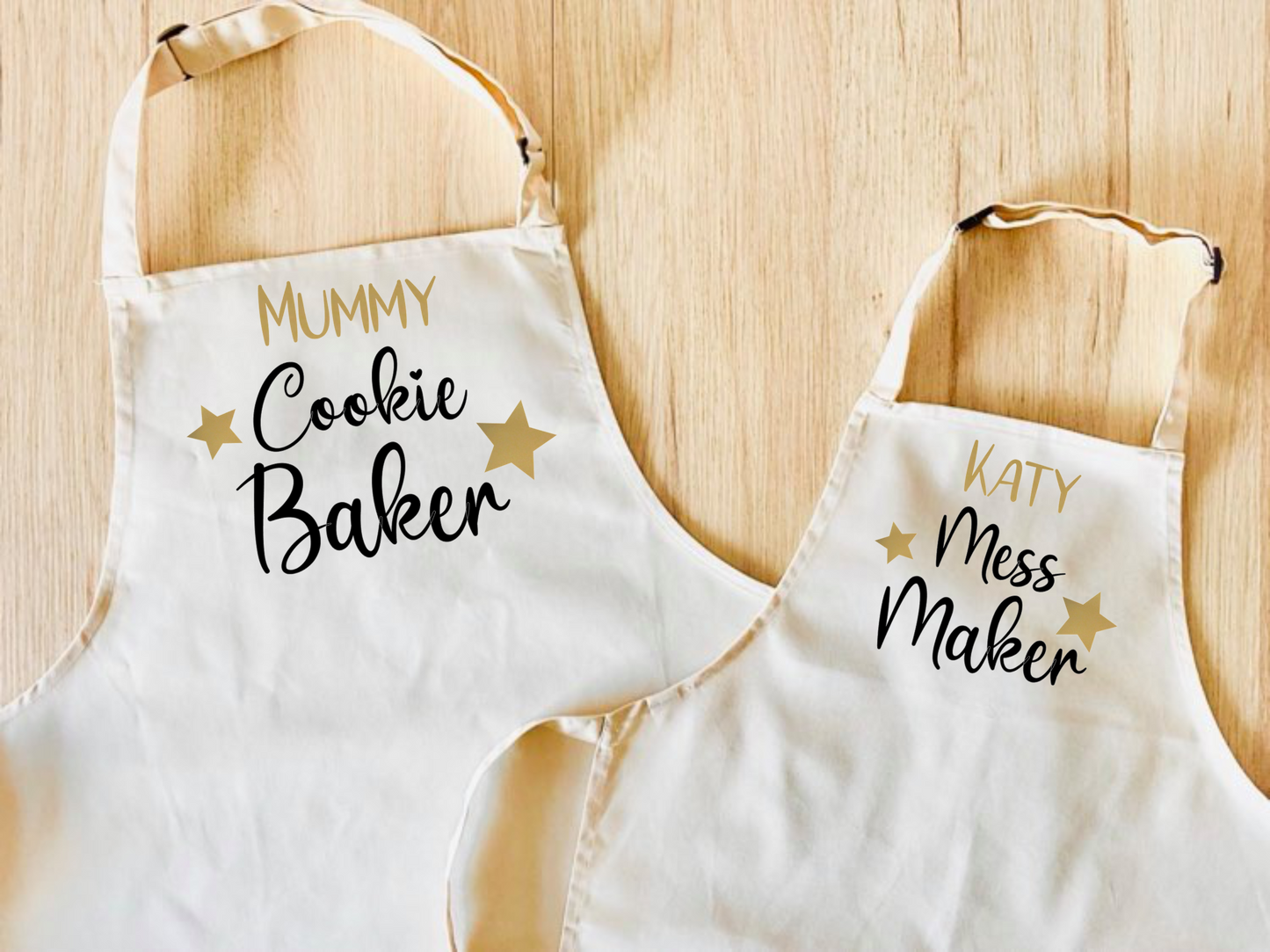 set of 2 personalised aprons in a choice of colours. One has Cookie Baker on it, the other has Mess Maker on it.